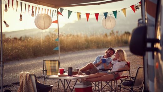 Young couple  sitting  in front of camper van and drinking .Travel and friendship celebration concept