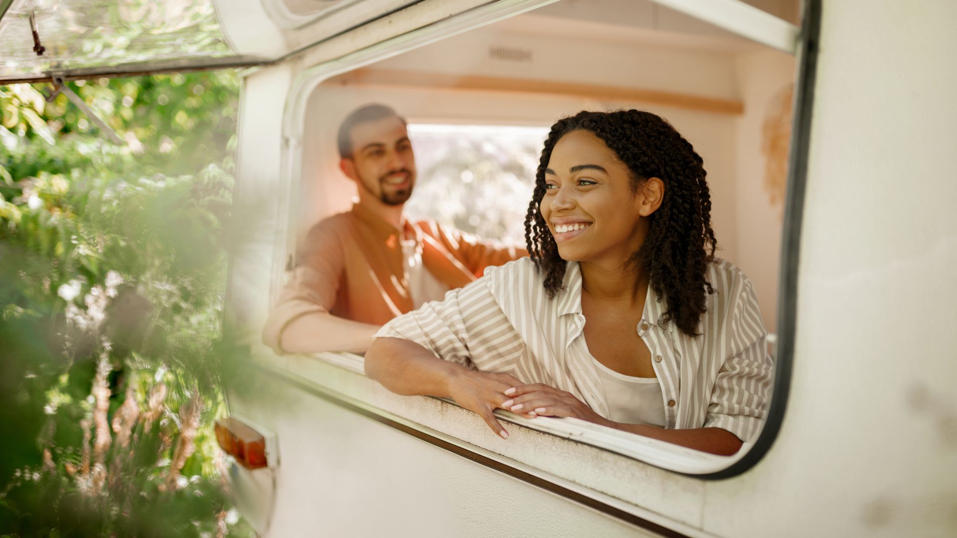 Husband and wife looks out of rv window, camping in a trailer. Man and woman travels on van, romantic vacations on motorhome, campers leisures in camping-car