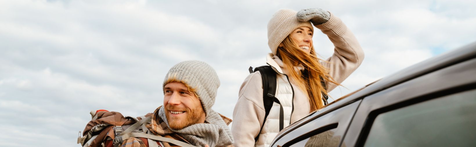 White happy couple with backpacks smiling together during car trip