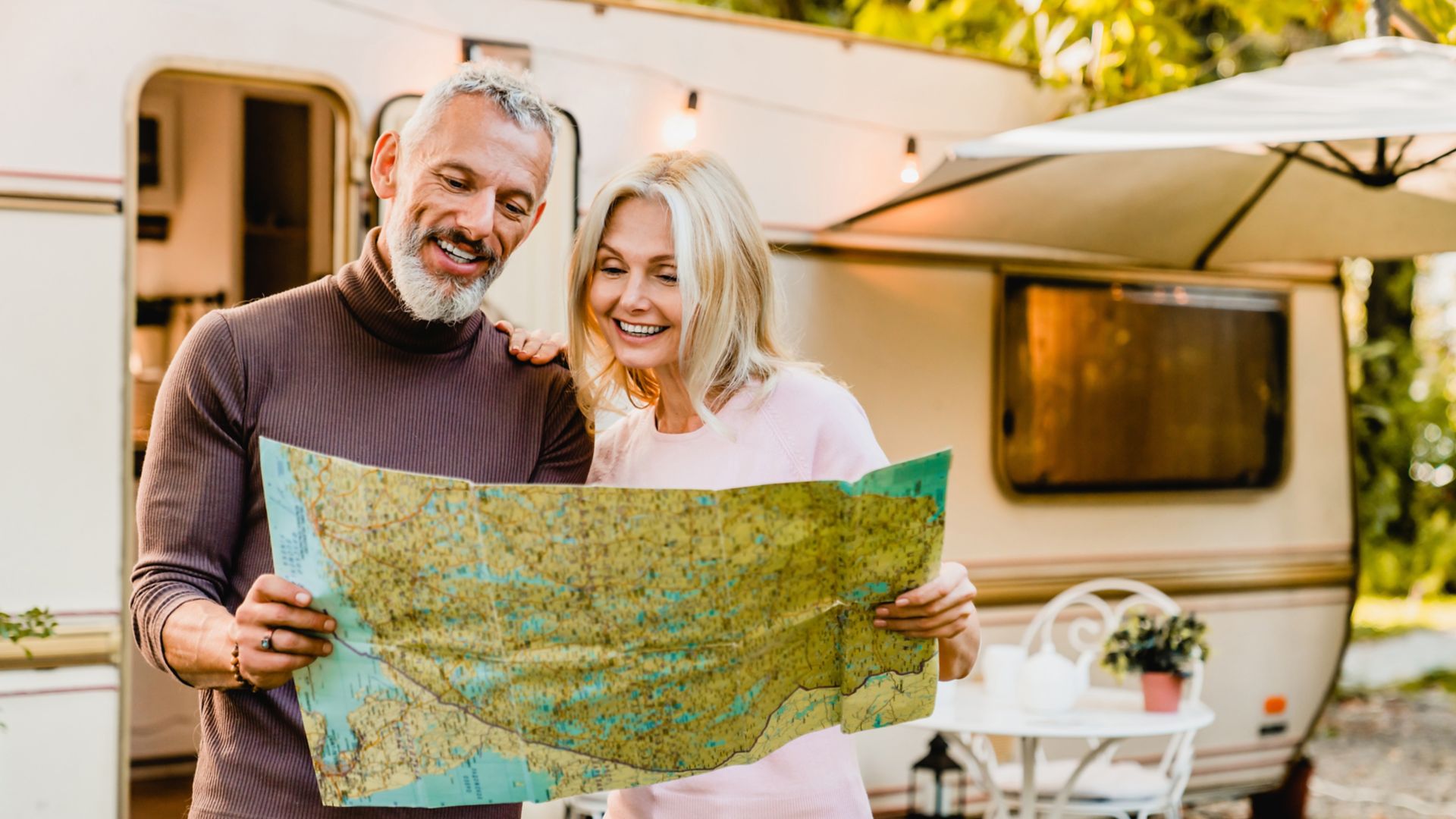 Energetic elderly european couple looking at the map with their caravan home behind