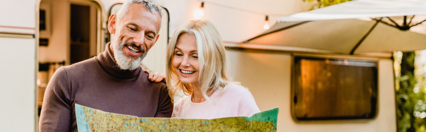 Energetic elderly european couple looking at the map with their caravan home behind