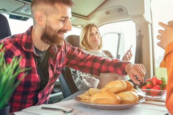 Happy friends having breakfast in a camper van in the morning