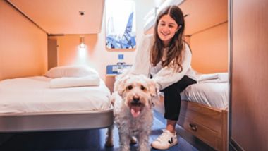 Meisje zit met een ruwharig wit hondje op een bed in een hut aan boord