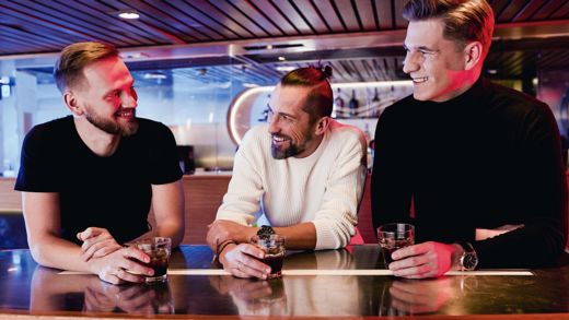 Uśmiechnięci mężczyźni stoją przy barze i piją.
