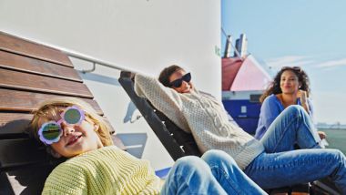 Oudere zus in een wit met blauw gestreepte zomerse jurk duwt haar jongere zus in een bloemmotief zomerse jurk op de schommel op het strand, dicht bij het water, op een bewolkte dag.