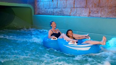 Två skrattande flickor på en blå uppblåsbar båt i vattenparken inomhus på Quality Hotel The Reef i Frederikshavn