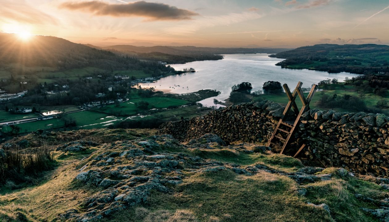 Sun rising above the horizon illuminating the landscape with stone wall and stile in foreground.