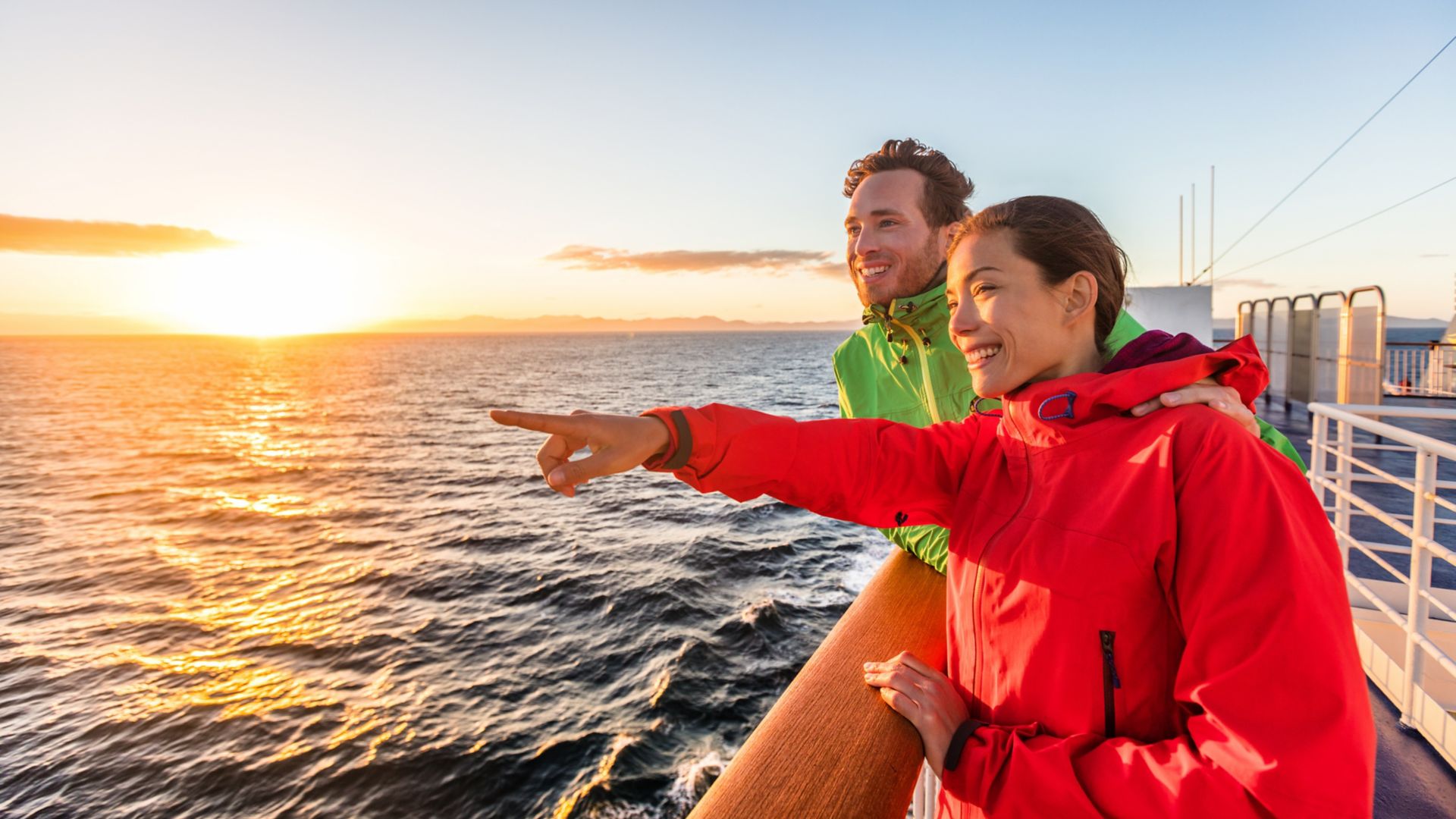 Kryssningsresor turister par pekar på havsutsikt från färjetur. Asiatisk kvinna multietniska människor reser tillsammans vid solnedgången.