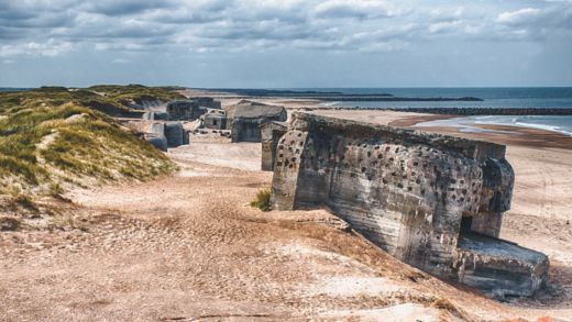 Sandstrand med en stor klippa och rester av en bunker