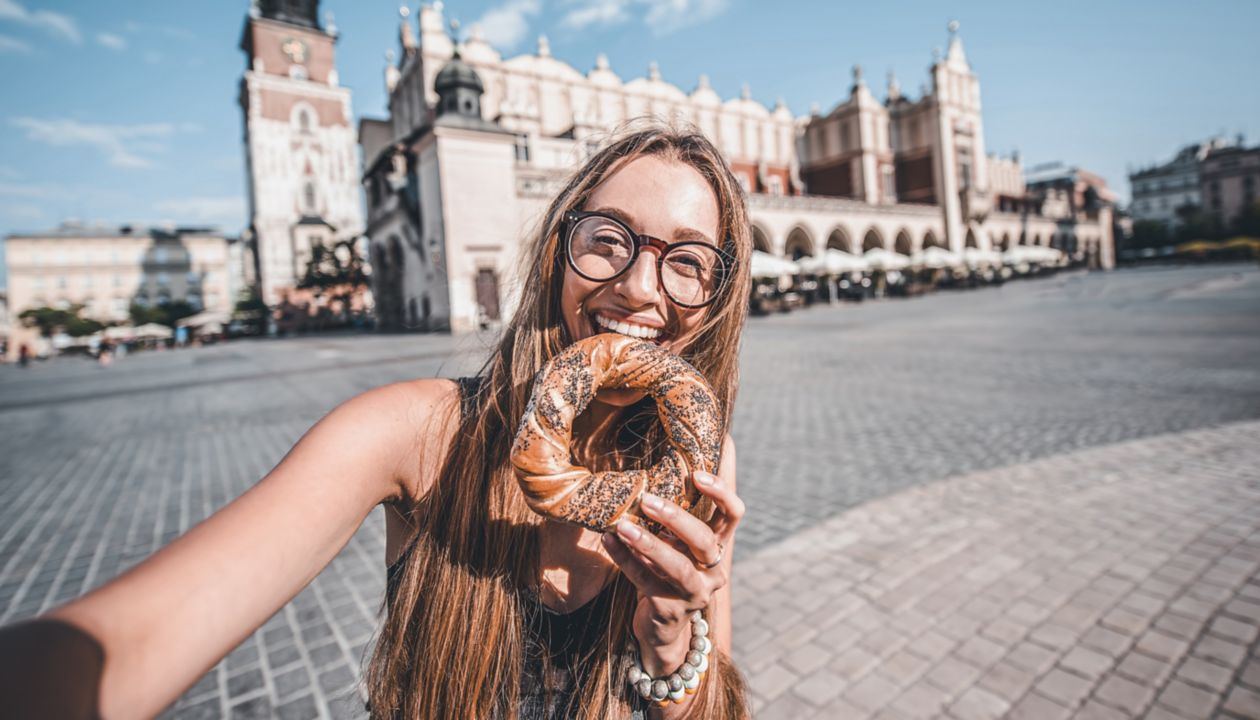 Young woman tourist eating prezel on the market square in Krakow in Poland