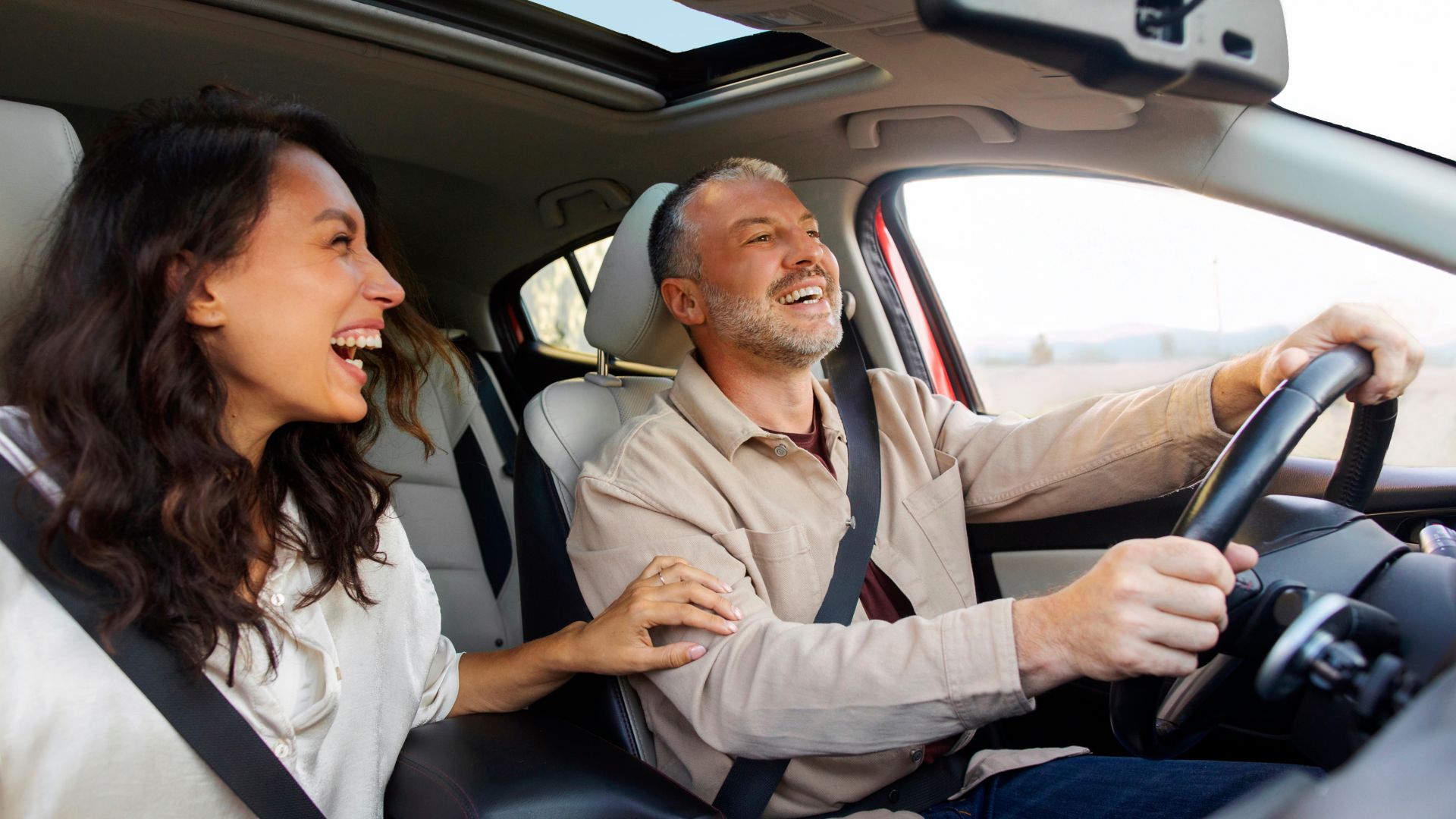 Excited woman laughing and joking with her happy husband while driving to vacation spot, spouses talking and enjoying road trip