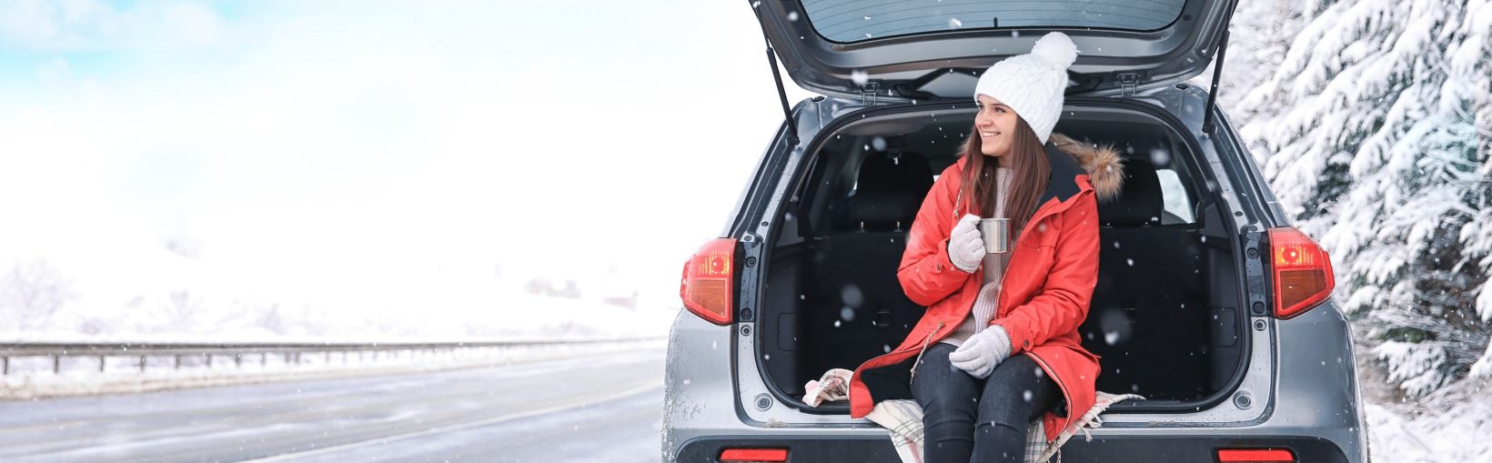 Female tourist drinking tea near car in snowy countryside