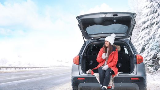 Female tourist drinking tea near car in snowy countryside