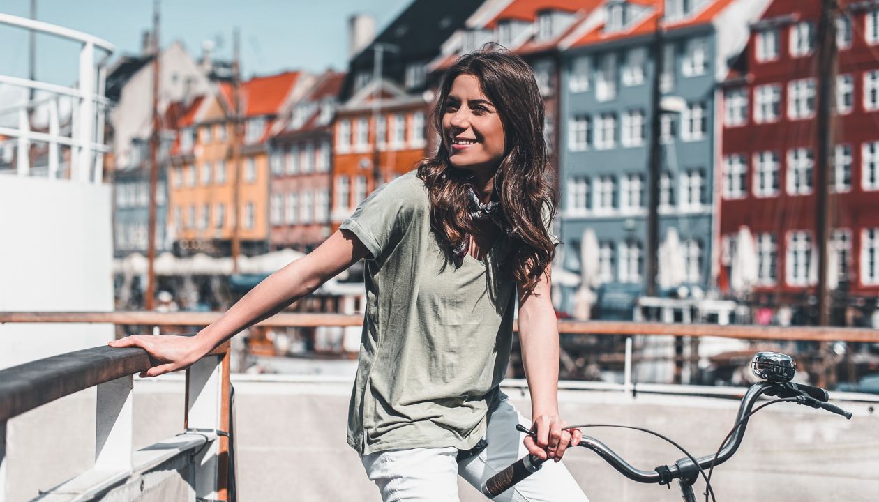 Lovely young woman posing with bike at the Nyhavn harbor pier in european city Copenhagen, Denmark, on sunny day. Visiting Scandinavia, famous European place.