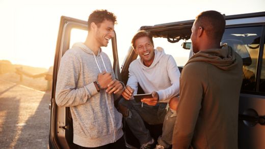 Three friends chatting outside a car in the sunset