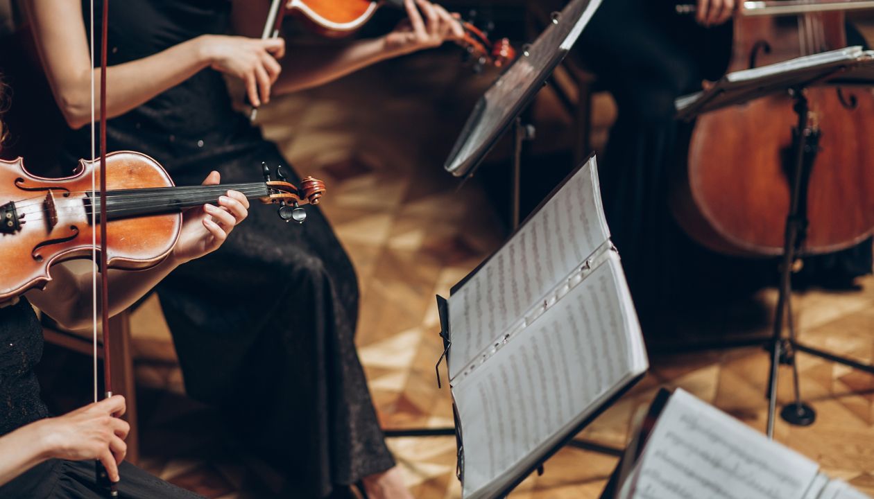 Elegant string quartet playing in luxury room at wedding reception in restaurant. group of people in black performing on violin and cello at theatre orchestra, music concept