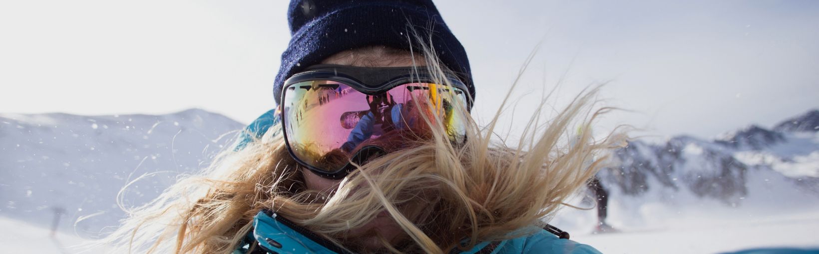 Cool woman makes photo selfie on smartphone on ski slopes in mountains, wears goggles for snow and sun