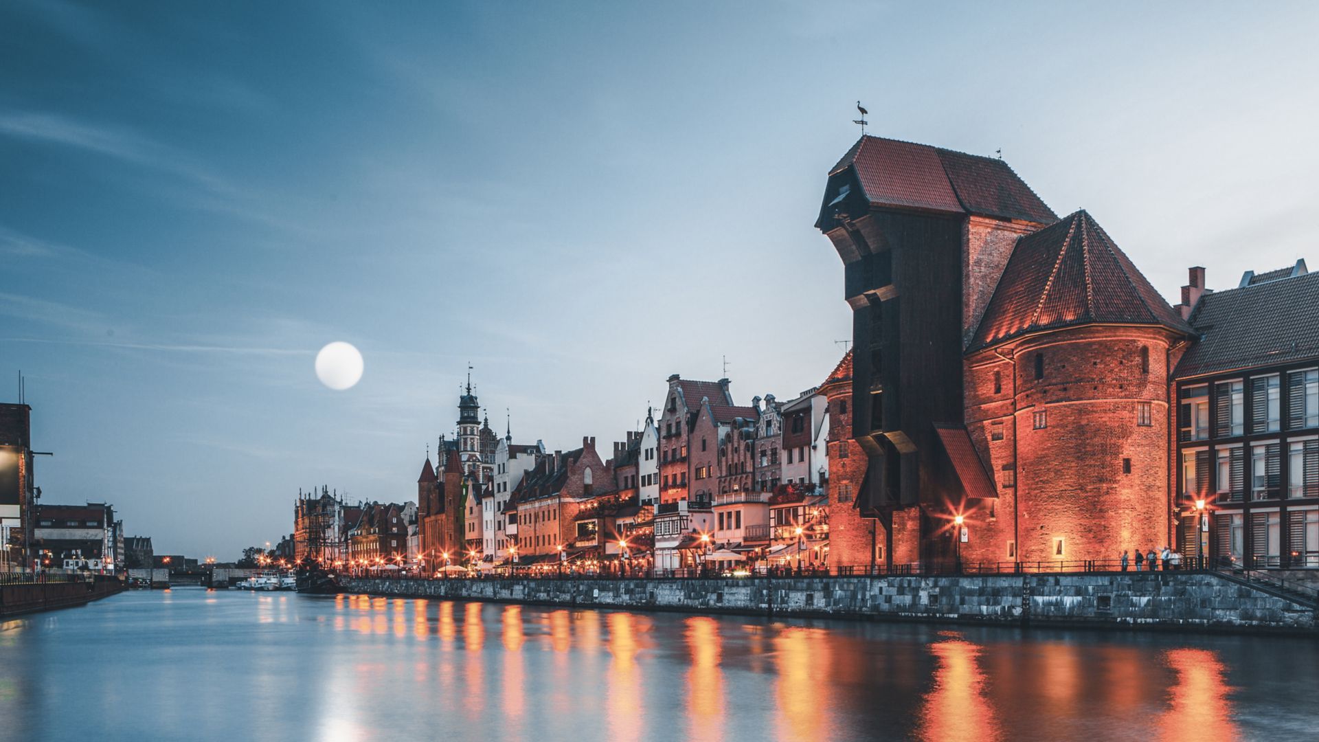 En vy över hamnen i gamla stan i Gdansk i skymningen visar de upplysta fasaderna på de traditionella byggnaderna.