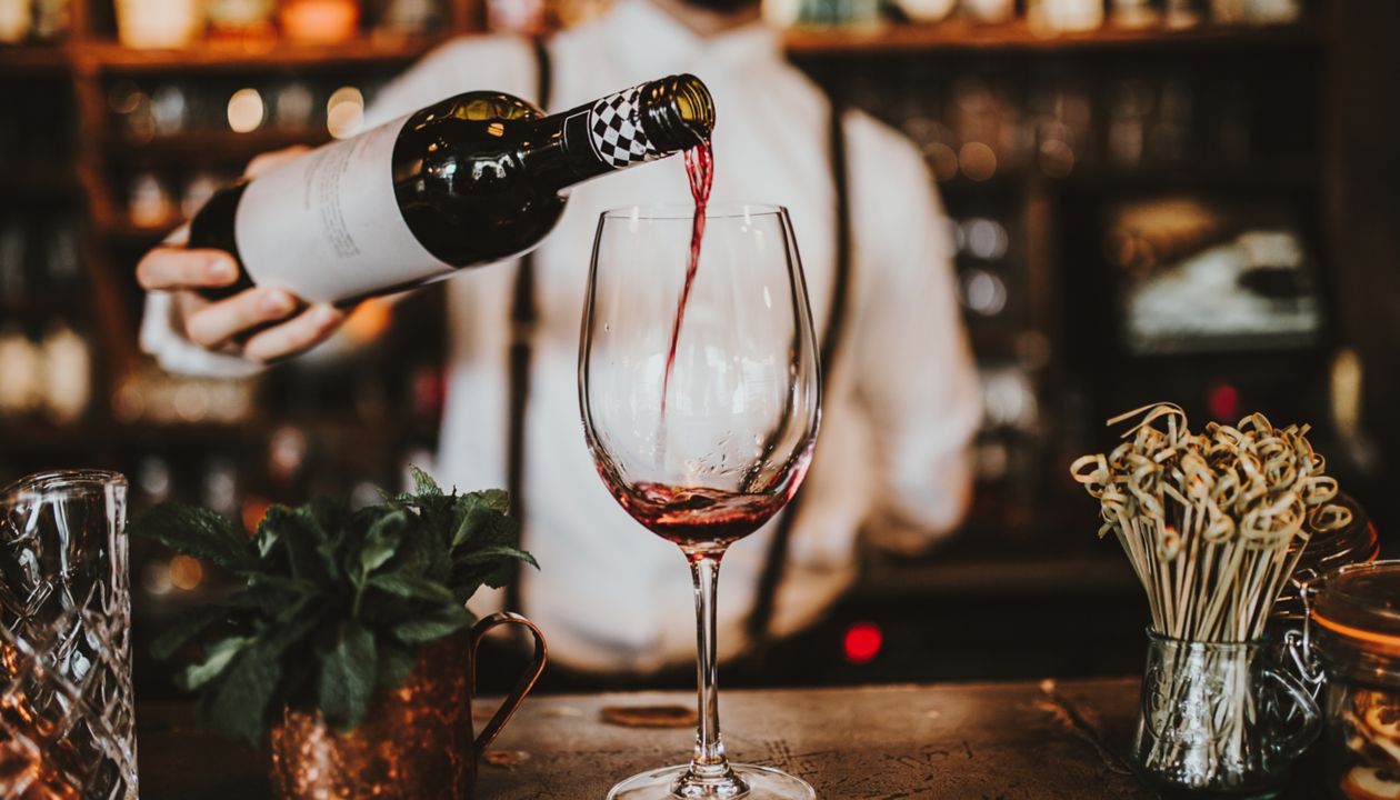 Iš arti kadras – barmenas į taurę pila raudoną vyną. Svetingumas, gėrimas ir vyno koncepcija. 