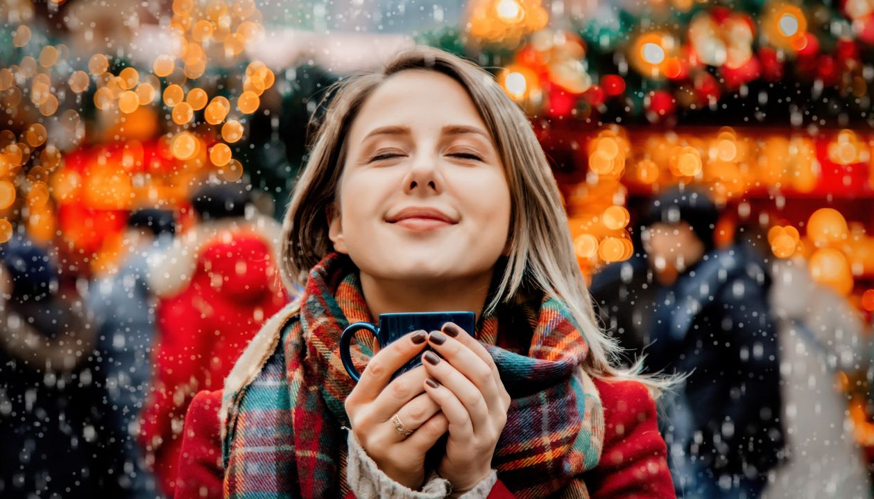 Una bella ragazza adulta con una tazza contenente una bevanda calda alla fiera di Natale a Dresda, Germania