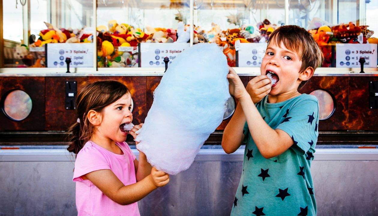 Photo of a brother and sister eating a big cotton candy at an amusement park.