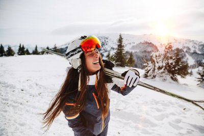 Smilende skiløber med ski på skulderen i et solbelyst, snedækket bjerglandskab i Norge.