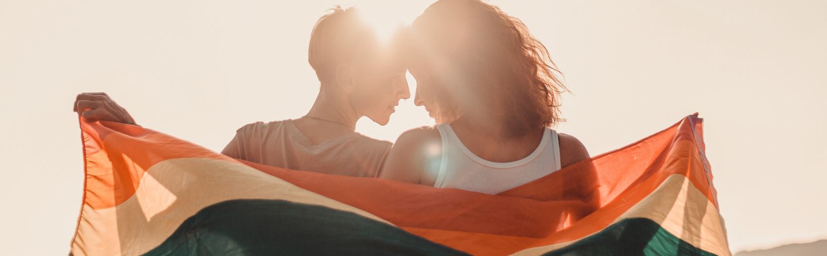 Et vakkert skeivt par i ung alder omfavner hverandre og holder et regnbueflagg, like rettigheter for LGBT-samfunnet,