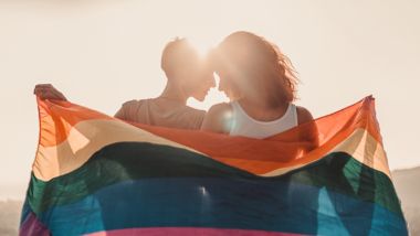 Skaists, jauns lesbiešu pāris mīloši apskaujas un tur varavīksnes karogu un zīmi par vienlīdzīgām tiesībām LGBT kopienai,