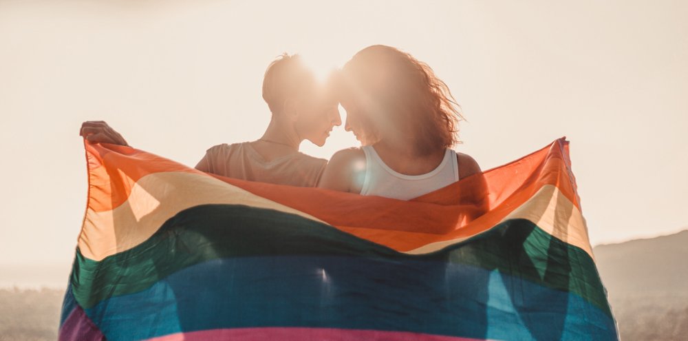 A beautiful lesbian young couple gently lovingly embraces and holds a rainbow flag, equal rights for lgbt community,