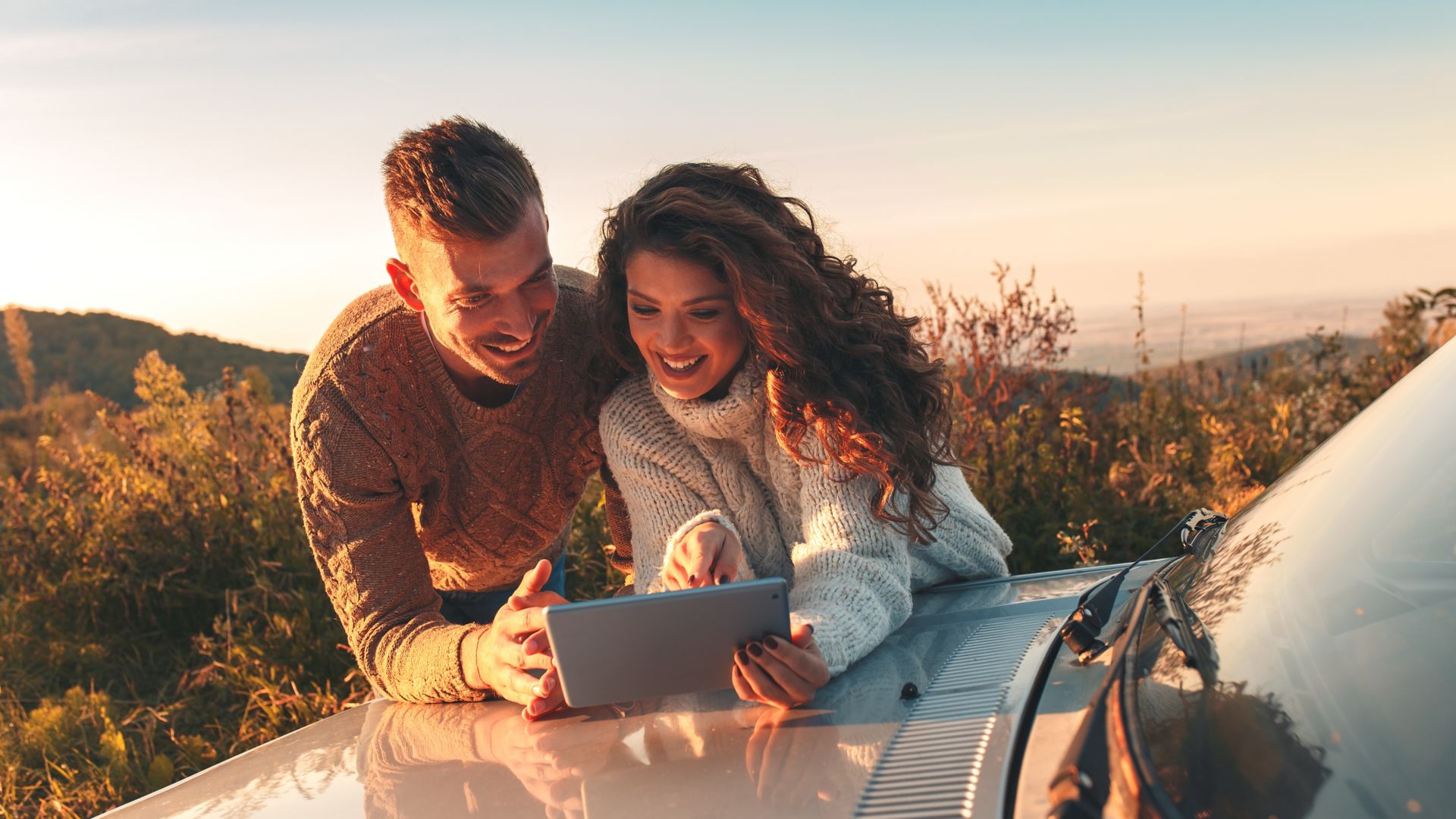 Beautiful couple on road trip, they are taking a break from driving and looking for direction on tablet.