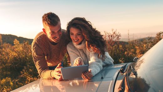 Beautiful couple on road trip, they are taking a break from driving and looking for direction on tablet.