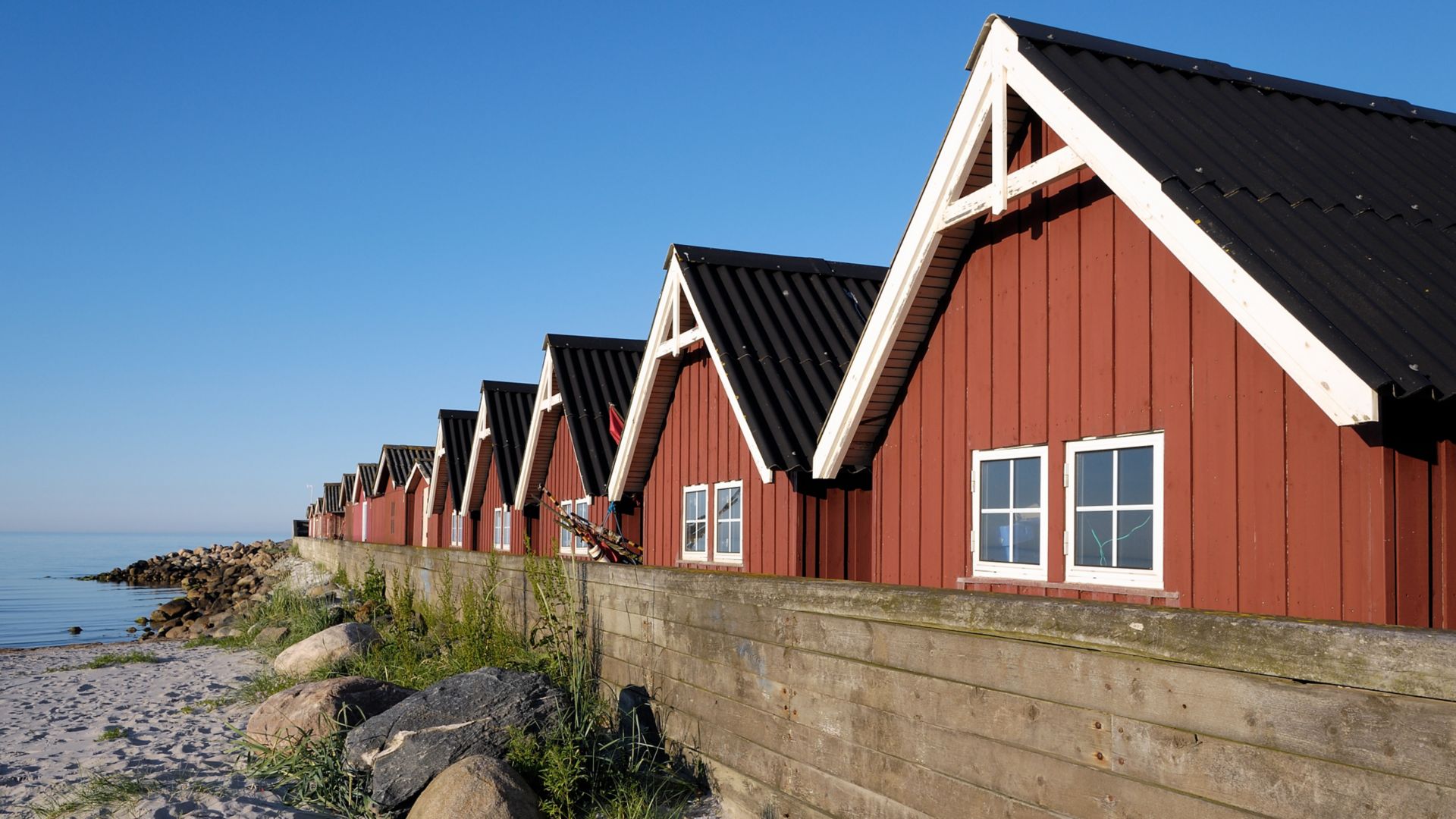 Red walled fishing huts backing on to a small beach at Strandby Harbour in Denmark.