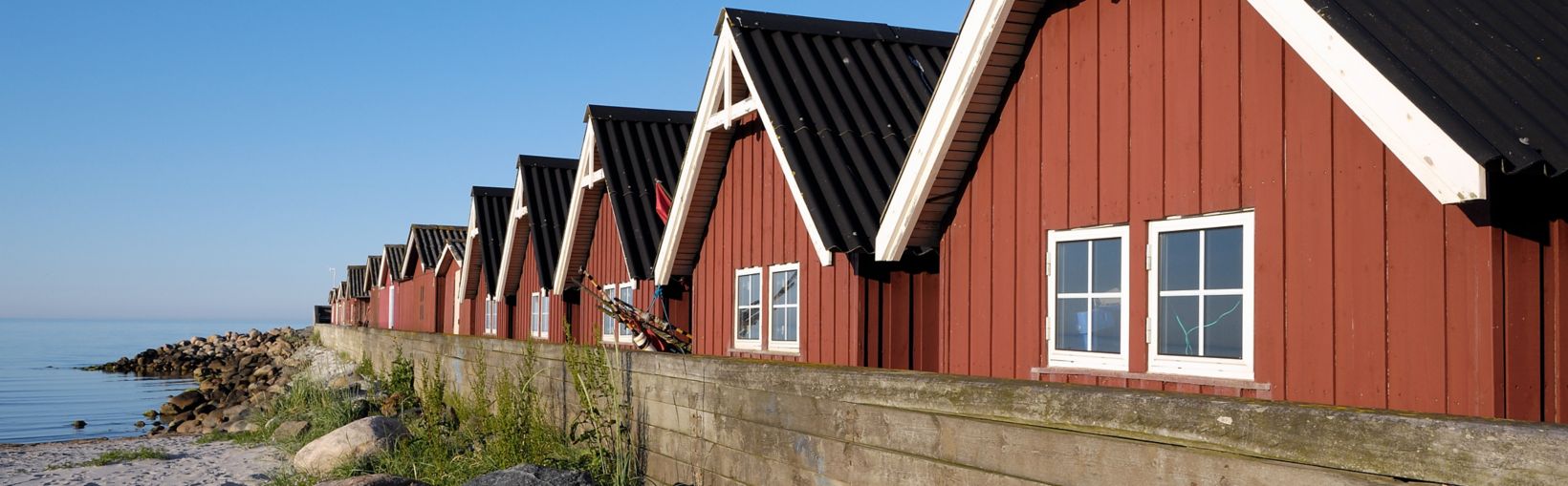 Red walled fishing huts backing on to a small beach at Strandby Harbour in Denmark.