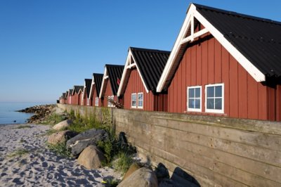 Red walled fishing huts backing on to a small beach at Strandby Harbour in Denmark.