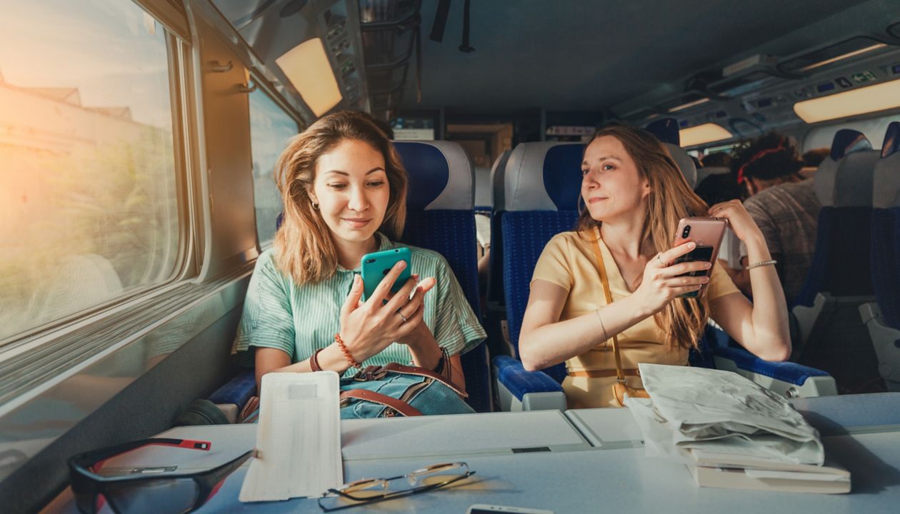 Happy two female friends travelling by long distant high speed train using their smartphones