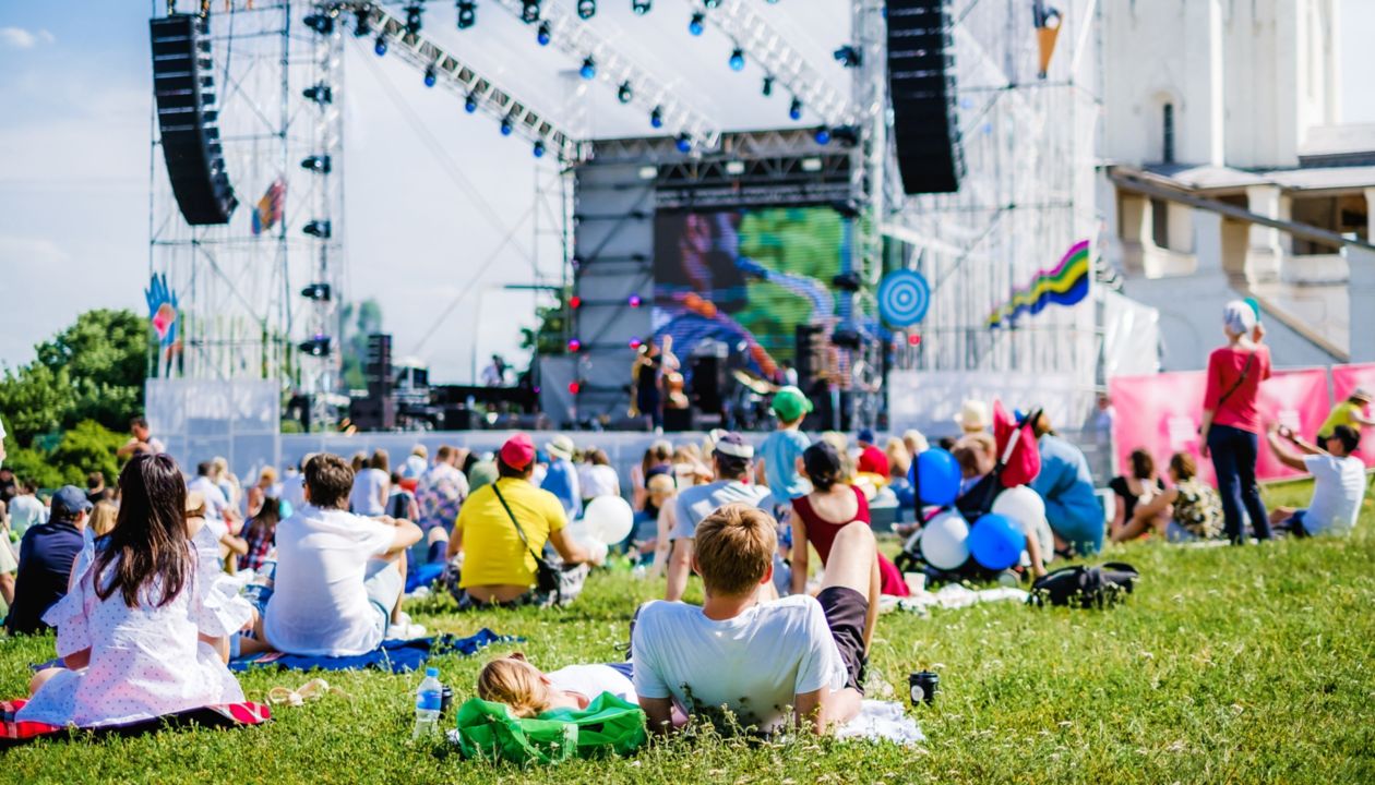 Pareja viendo un concierto en festival de música al aire libre, vista posterior, escenario y espectadores al fondo