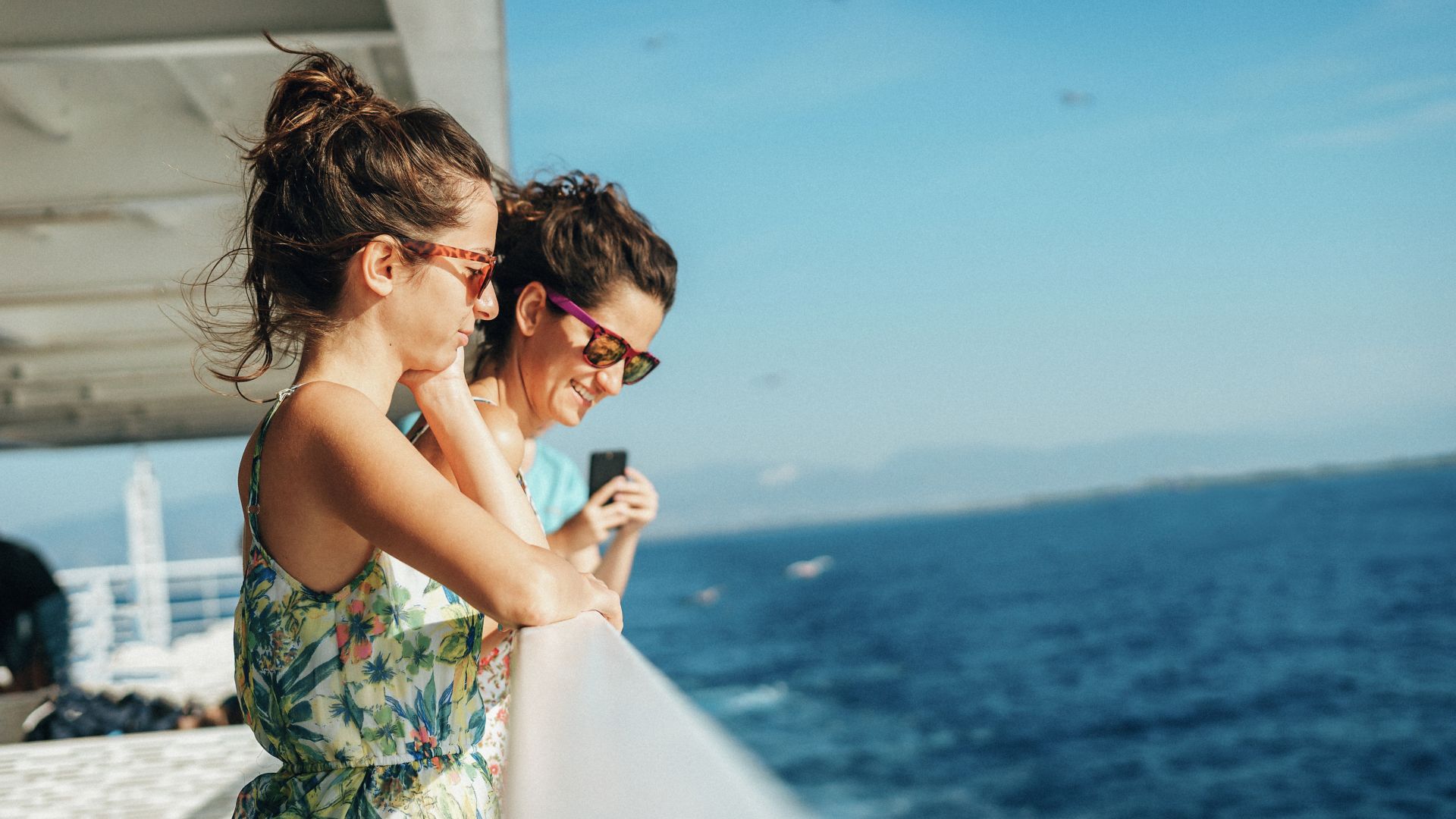 wo young women girl friends sisters standing by the fence on deck of the ferry