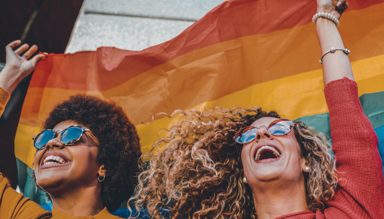 Two women friends hanging out in the city waving LGBT with pride flag