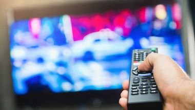 Young man holding television remote control. Hands pointing to tv screen set and turning it on or off select channel watching tv on his sofa at home in the living room relax.