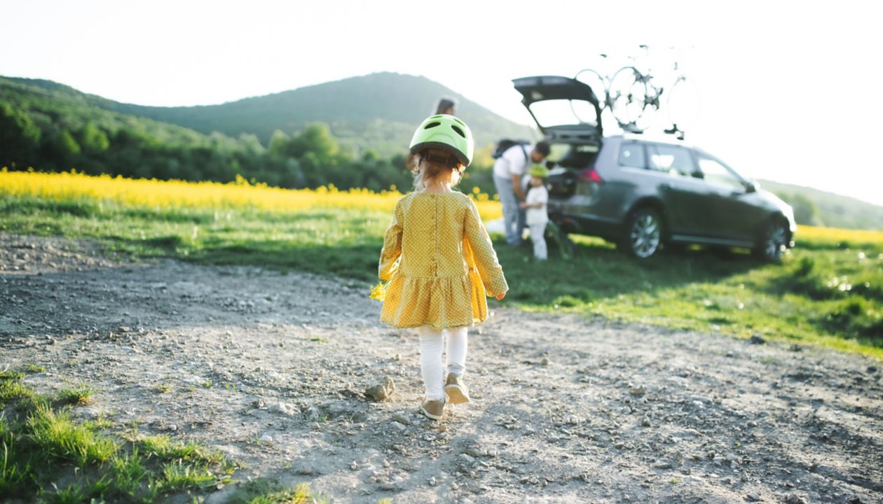 Vista posteriore di una bambina con la famiglia che fa una gita in bicicletta in campagna, camminando.