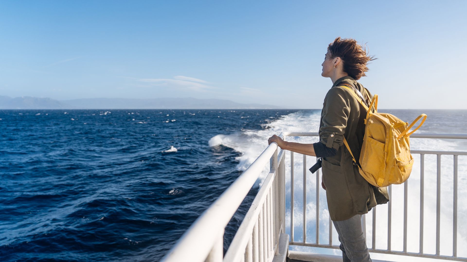 Side view of pensive short haired woman standing on ship deck and looking at waves in sunlight