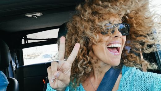 Travel with car and happiness - joyful beautiful adult woman enjoy travel and have fun looking outside the open window with wind on her blonde curly long hair - female people smile and laugh traveling