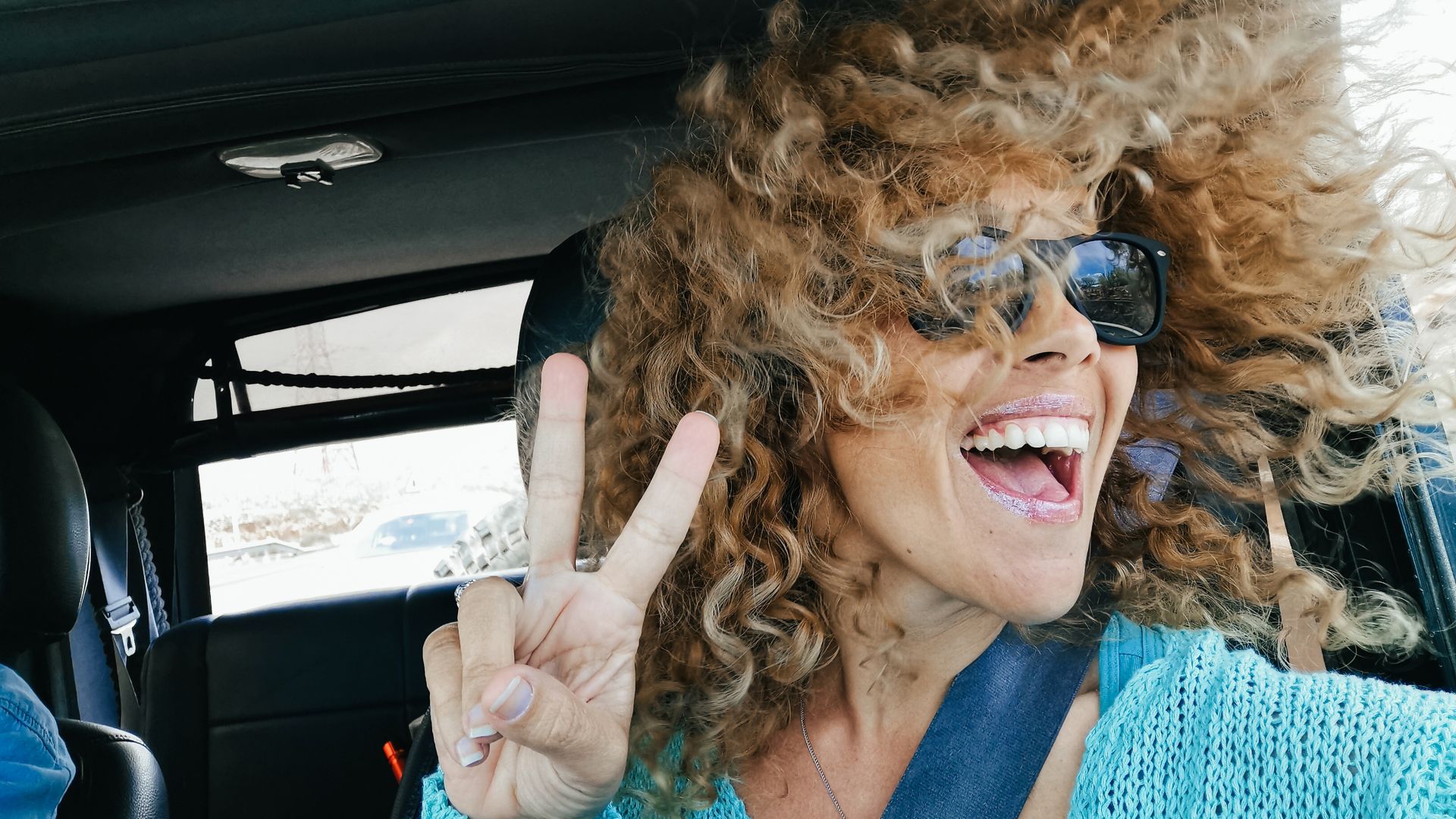 Travel with car and happiness - joyful beautiful adult woman enjoy travel and have fun looking outside the open window with wind on her blonde curly long hair - female people smile and laugh traveling