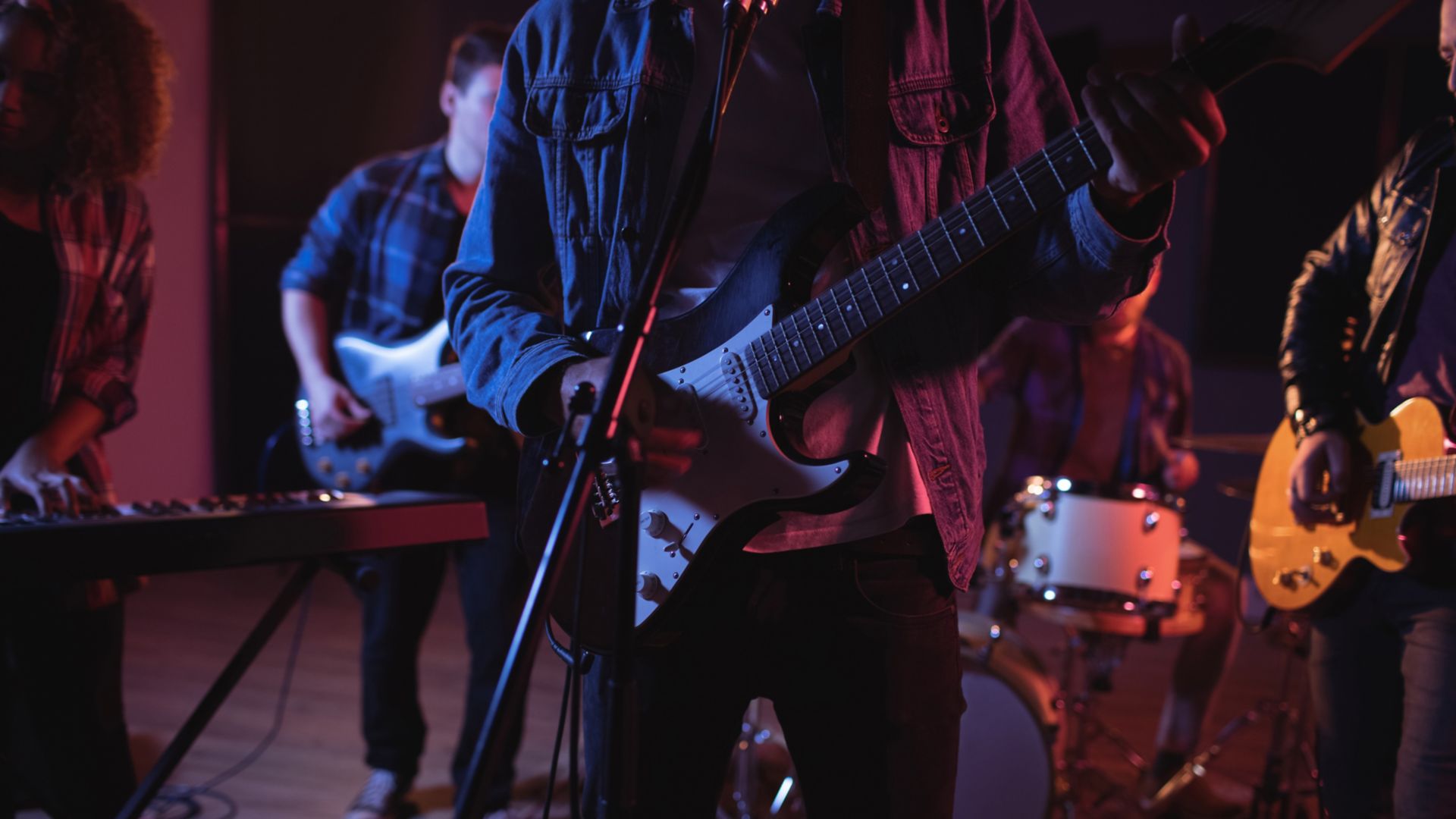 Midsection of diverse music band with guitarists and keyboard player during concert in music venue