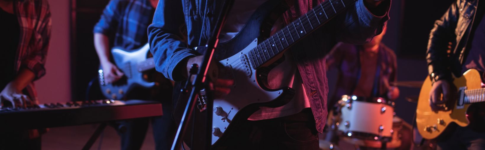 Midsection of diverse music band with guitarists and keyboard player during concert in music venue