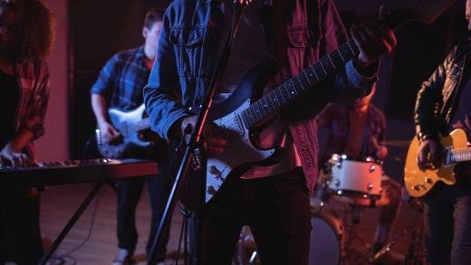 Midsection of diverse music band with guitarists and keyboard player during concert in music venue