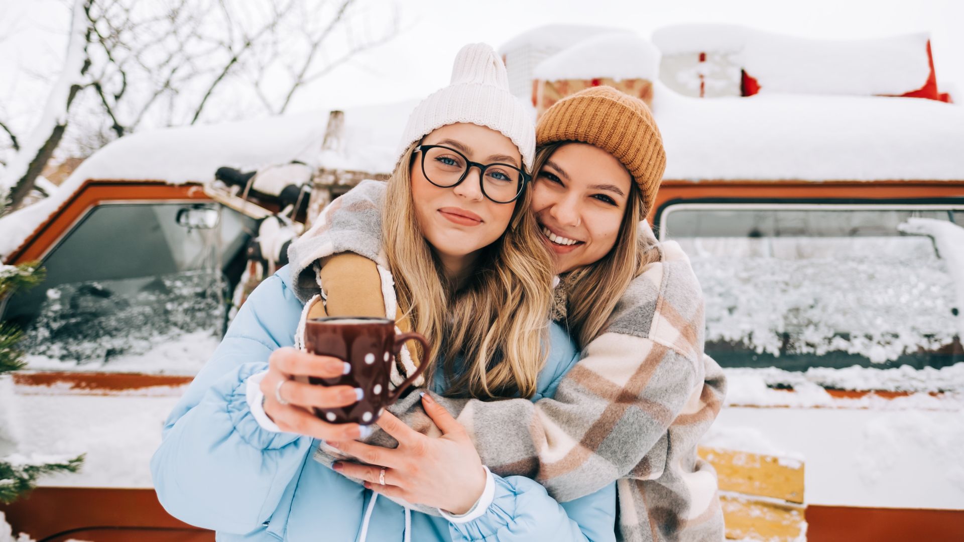 Portrait of two cheerful women friends heaving fun standing outdoor near van, enjoying winter time.