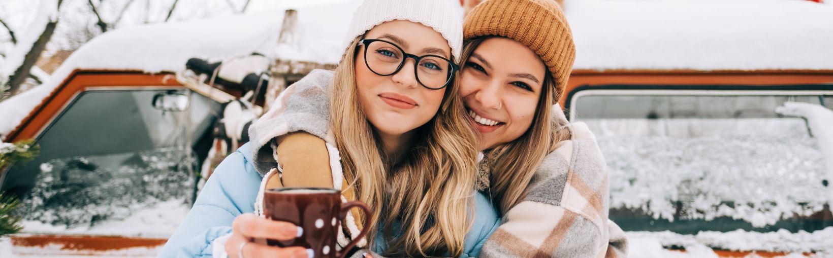 Portrait of two cheerful women friends heaving fun standing outdoor near van, enjoying winter time.