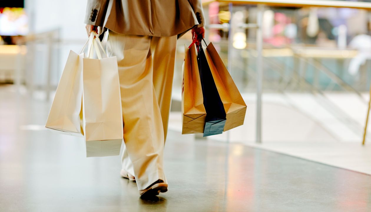 Low section of unrecognizable woman wearing pants and holding blank shopping bags while walking in mall, copy space