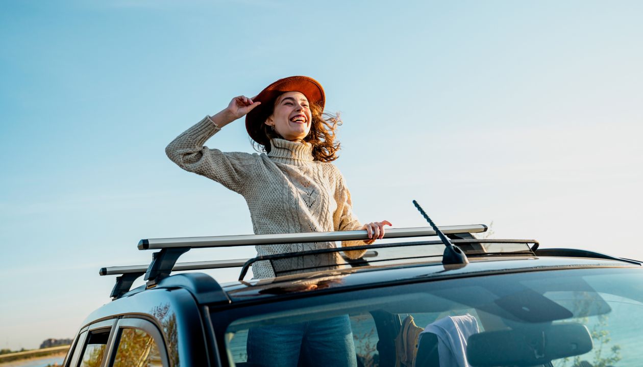 Cheerful young woman wearing hat enjoying through sun roof of car